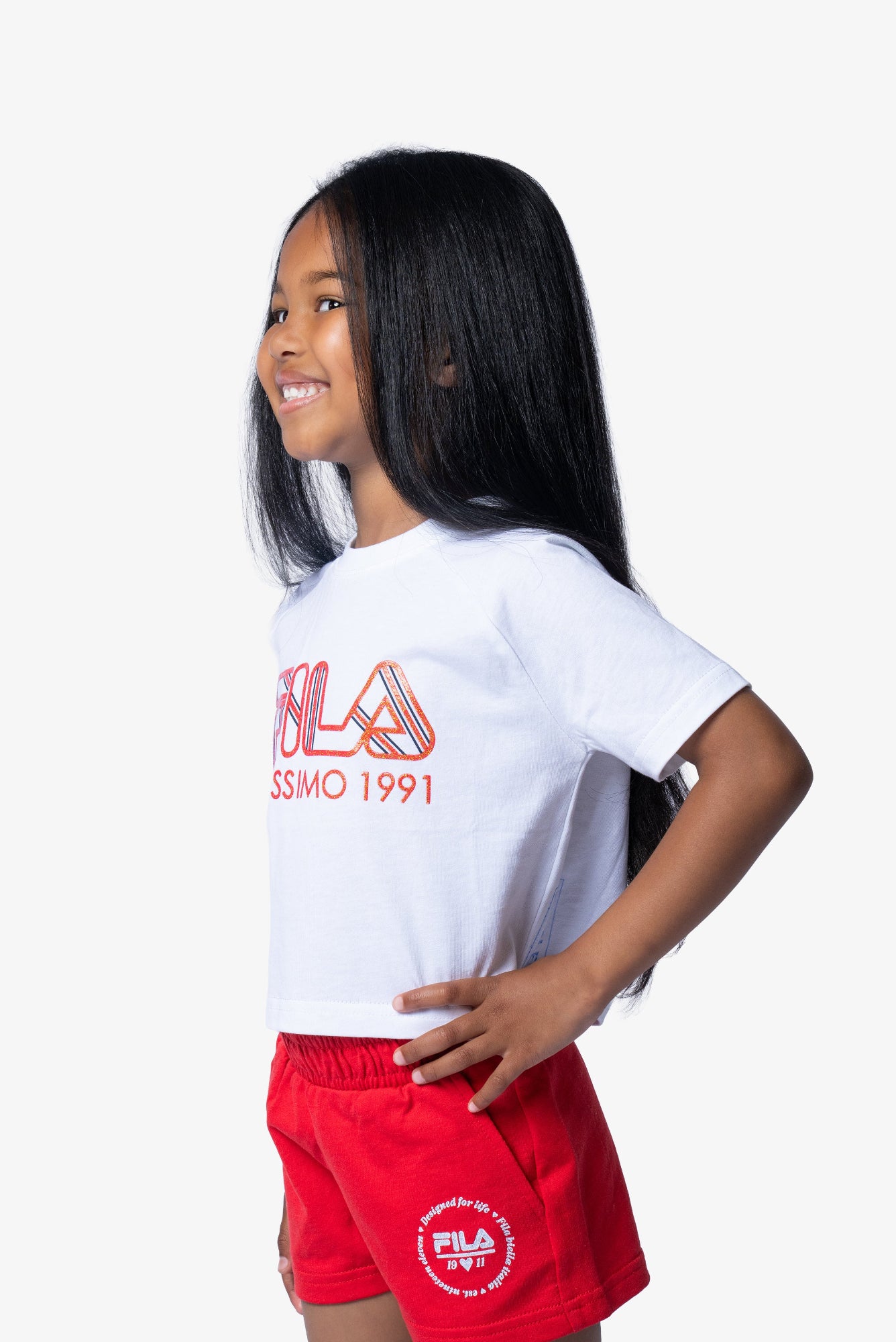Child wearing a white FILA t-shirt and red shorts on a white background
